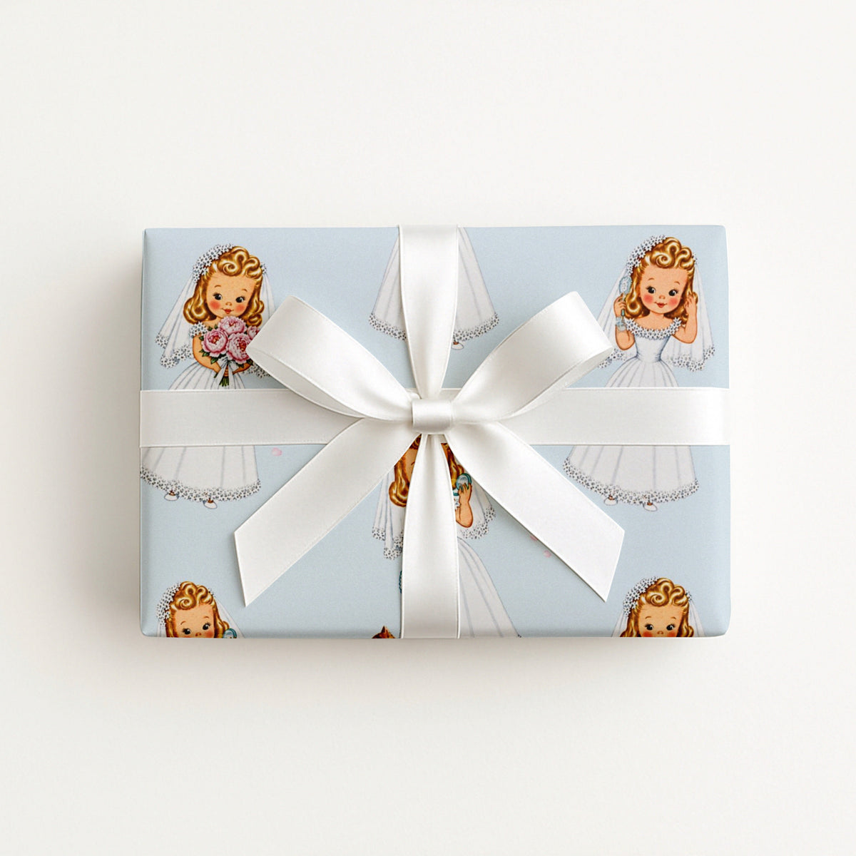 A rectangular gift box wrapped in light blue wrapping paper with a repeating vintage illustration of a darling bride with a bouquet of peonies, and a large white ribbon bow, photographed against a clean white background.