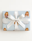 A rectangular gift box wrapped in light blue wrapping paper with a repeating vintage illustration of a darling bride with a bouquet of peonies, and a large white ribbon bow, photographed against a clean white background.