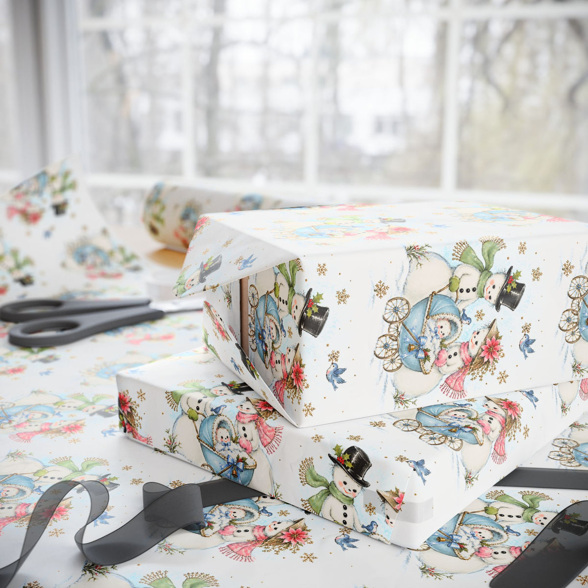 Stacked Christmas gifts wrapped in vintage-style snowman baby boy wrapping paper with a blue baby carriage on a wrapping table with scissors and black ribbon
