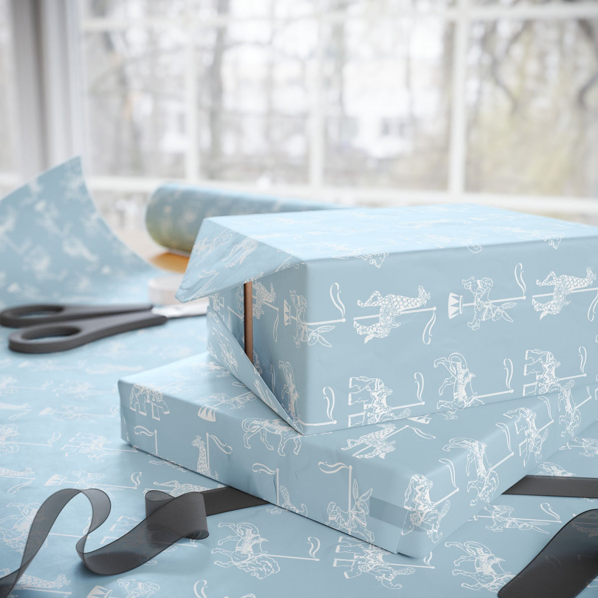 Light blue wrapping paper with a white line-art illustration pattern of carousel animals, shown wrapped around gift boxes on a table near a window, with scissors and ribbon visible.