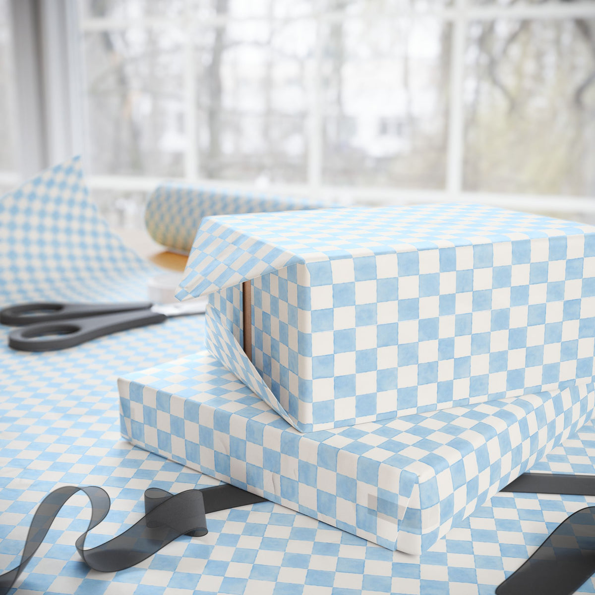 Light blue and white checkered wrapping paper wrapped around gift boxes on a table, with scissors and ribbon visible in a softly lit indoor setting.