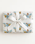 A rectangular gift box wrapped in white paper with a repeating pattern of vintage blue airplanes carrying a boy pilot, tied with a wide white ribbon and bow, on a light off-white background.