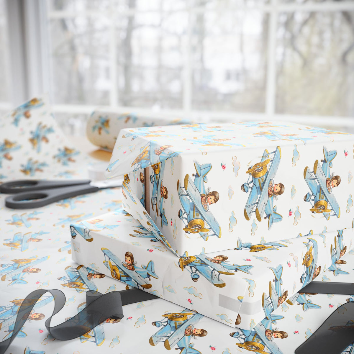 Gift-wrapped boxes and wrapping paper with a repeating airplane-and-child pattern, styled on a table near scissors and a window.