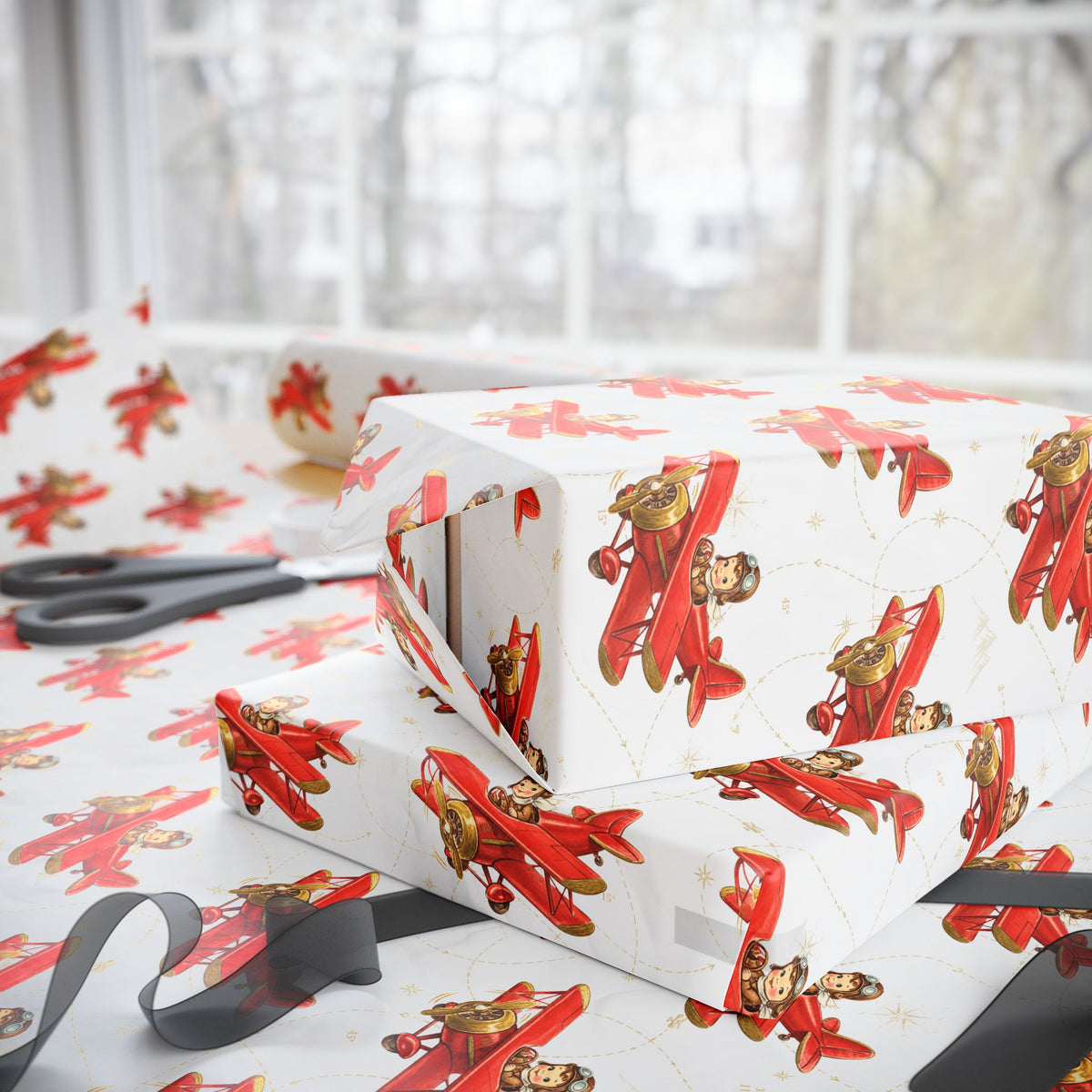 Gift boxes wrapped in paper featuring a little boy flying a red biplane over a delicate aviation navigation map on an ivory background, displayed with an open roll of matching wrapping paper, dark ribbon, and scissors.
