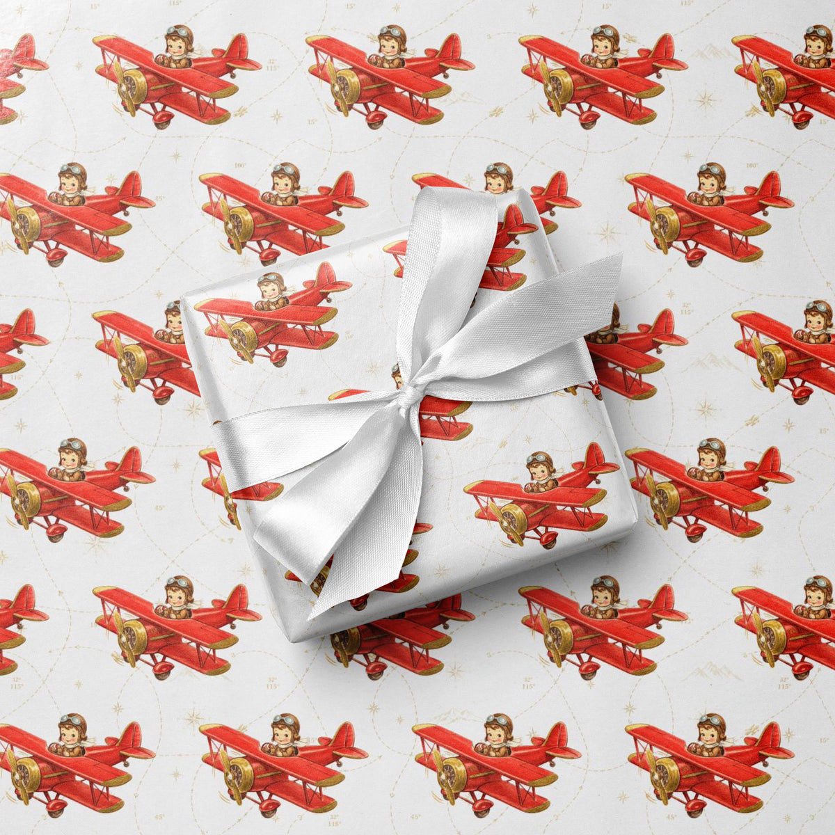 Wrapped gift tied with a white satin bow, displayed on matching wrapping paper featuring a little boy piloting a red airplane over a delicate navigation map with gold accents on an ivory background.