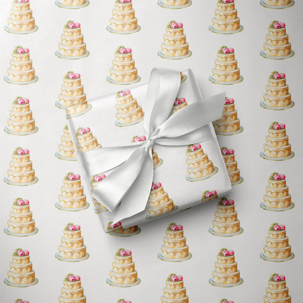 Gift wrapped in elegant wedding cake wrapping paper with a white satin bow, resting on a sheet of the repeating tiered cake pattern