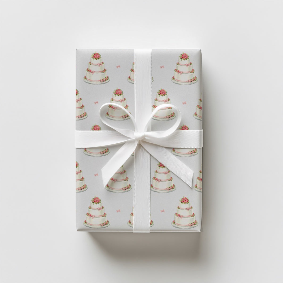 Gift wrapped in minimalist wedding cake wrapping paper with tiered cakes and pink roses, tied with a white satin ribbon and bow