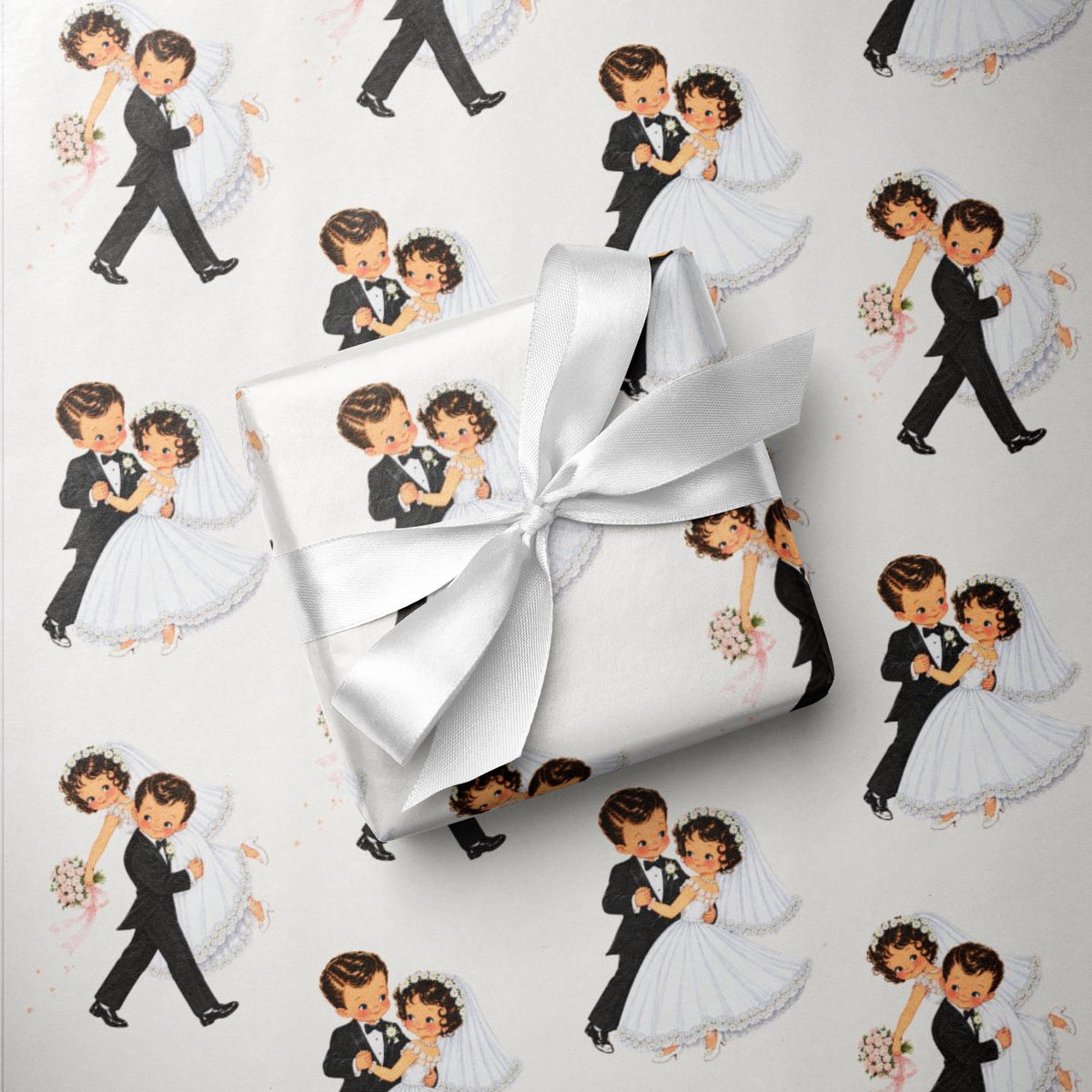 A gift box wrapped in ivory wedding wrapping paper featuring a repeating pattern of vintage bride and groom couples, tied with a white satin ribbon, on a white background.