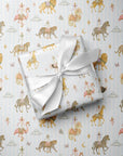 A wrapped gift box tied with a white satin ribbon, placed on top of pale blue wrapping paper printed with a whimsical carousel and animal pattern in soft gold, pink, and brown tones.