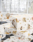 Stack of gifts wrapped in Carousel Menagerie wrapping paper featuring whimsical carousel animals on soft pink stripes, shown with matching gift wrap and ribbon.