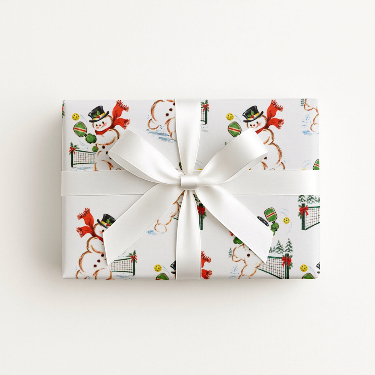 christmas gift wrapped in white paper with a repeating illustration that features different snowmen playing pickleball in the snow.