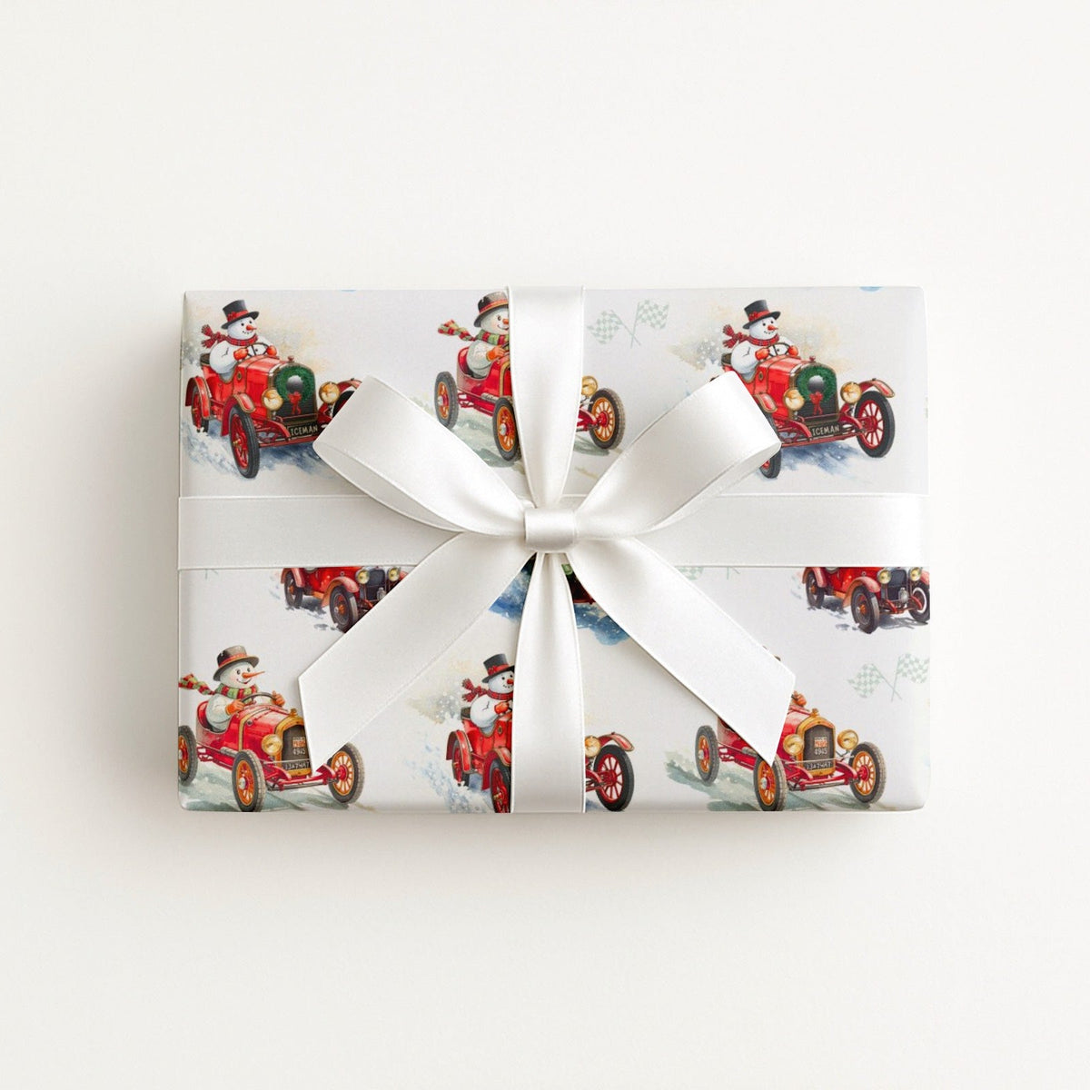 Flat lay of a gift wrapped in vintage-style snowman race car Christmas wrapping paper with a white satin bow