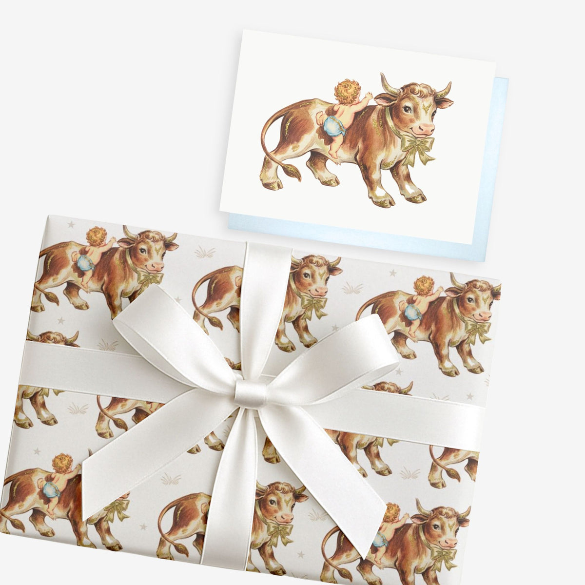 Vintage-style cowboy baby boy greeting card with a baby riding a farm bull, shown with matching gift wrap tied with a white satin bow