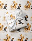 Illustrated cowboy wedding gift wrap pattern: a bride in a lace veil rides a golden horse and swings a lasso as her groom dashes ahead holding his hat.