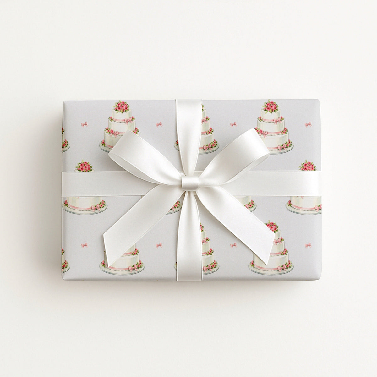 Flat lay of a gift wrapped in minimalist wedding cake wrapping paper with a large white satin bow