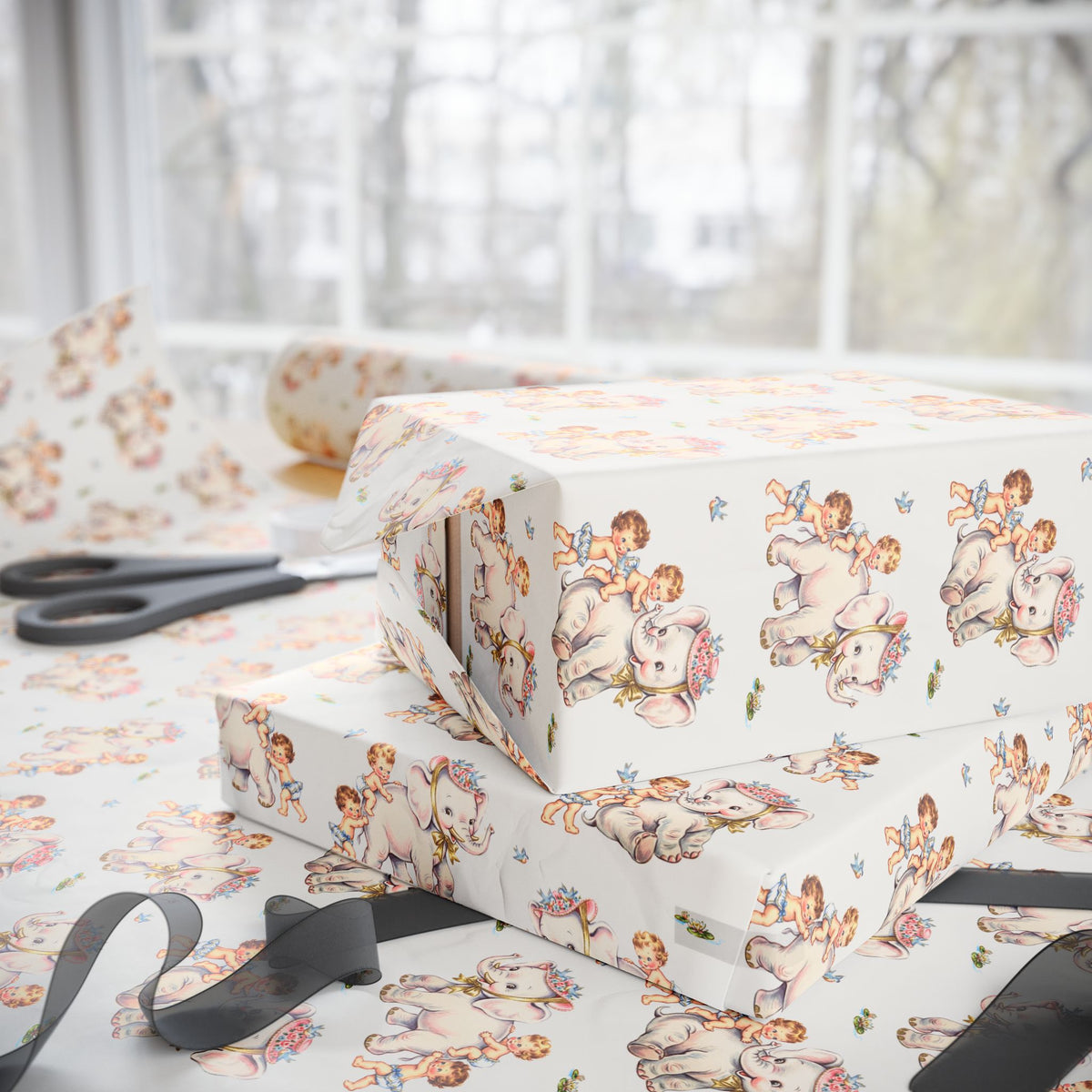 Ivory wrapping paper with a vintage style baby and elephant pattern, shown wrapped around gift boxes on a table with scissors and ribbon near a softly blurred window background.