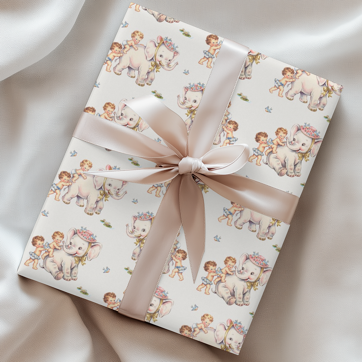 A rectangular gift box wrapped in cream wrapping paper with a repeating pattern of elephants and babies,  tied with a wide satin ribbon in a bow.
