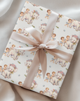 A rectangular gift box wrapped in cream wrapping paper with a repeating pattern of elephants and babies,  tied with a wide satin ribbon in a bow.