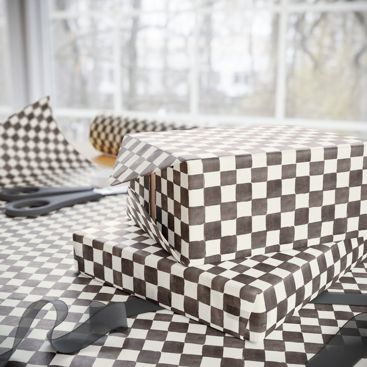 A gift box wrapped in brown and white checkered wrapping paper, with a matching sheet and ribbon on a table in front of a softly blurred window.