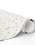 A roll of wrapping paper with a delicate pastel pattern of flowers, stars, and geometric shapes in pink, light blue, and gold on an off-white background, shown on a clean white studio background.