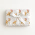 Vintage-style giraffe baby girl wrapping paper on a gift tied with a satin bow, baby girls riding giraffes in floral bonnets