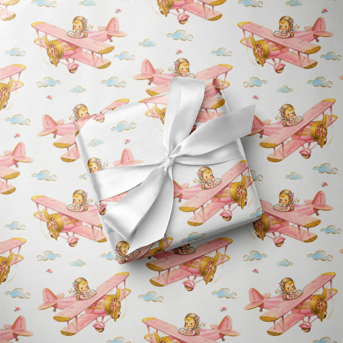 Flat lay of baby girl airplane wrapping paper with a wrapped gift tied with a white satin ribbon.