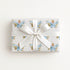 Wrapped gift in vintage-inspired airplane wrapping paper featuring a little girl flying a powder blue biplane over a delicate navigation map with gold accents on an ivory background, tied with a white satin bow.