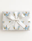 Wrapped gift in vintage-inspired airplane wrapping paper featuring a little girl flying a powder blue biplane over a delicate navigation map with gold accents on an ivory background, tied with a white satin bow.