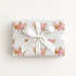 Wrapped gift in vintage-inspired airplane wrapping paper featuring a little girl flying a pastel pink biplane over a delicate navigation map with gold accents on an ivory background, tied with a white satin bow.