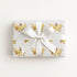 Wrapped gift in vintage-inspired airplane wrapping paper featuring a little girl flying a yellow and gold biplane over a delicate navigation map with gold accents on an ivory background, tied with a white satin bow.