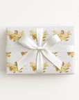 Wrapped gift in vintage-inspired airplane wrapping paper featuring a little girl flying a yellow and gold biplane over a delicate navigation map with gold accents on an ivory background, tied with a white satin bow.
