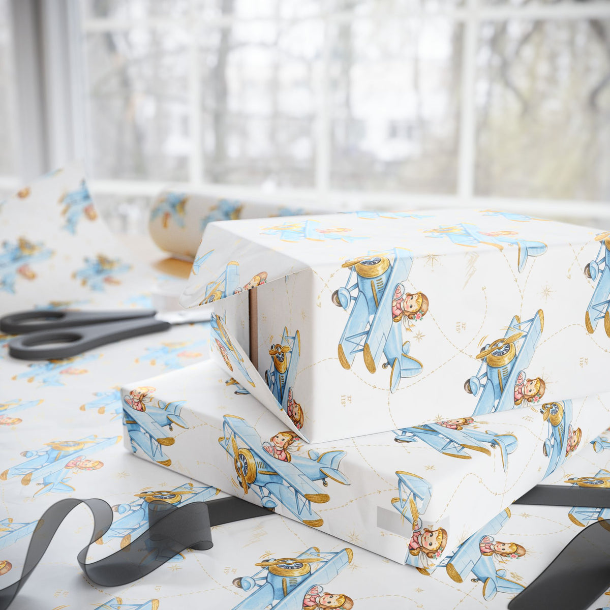 Gift boxes wrapped in paper featuring a little girl flying a powder blue biplane over a delicate aviation navigation map on an ivory background, displayed with an open roll of matching wrapping paper, dark ribbon, and scissors.