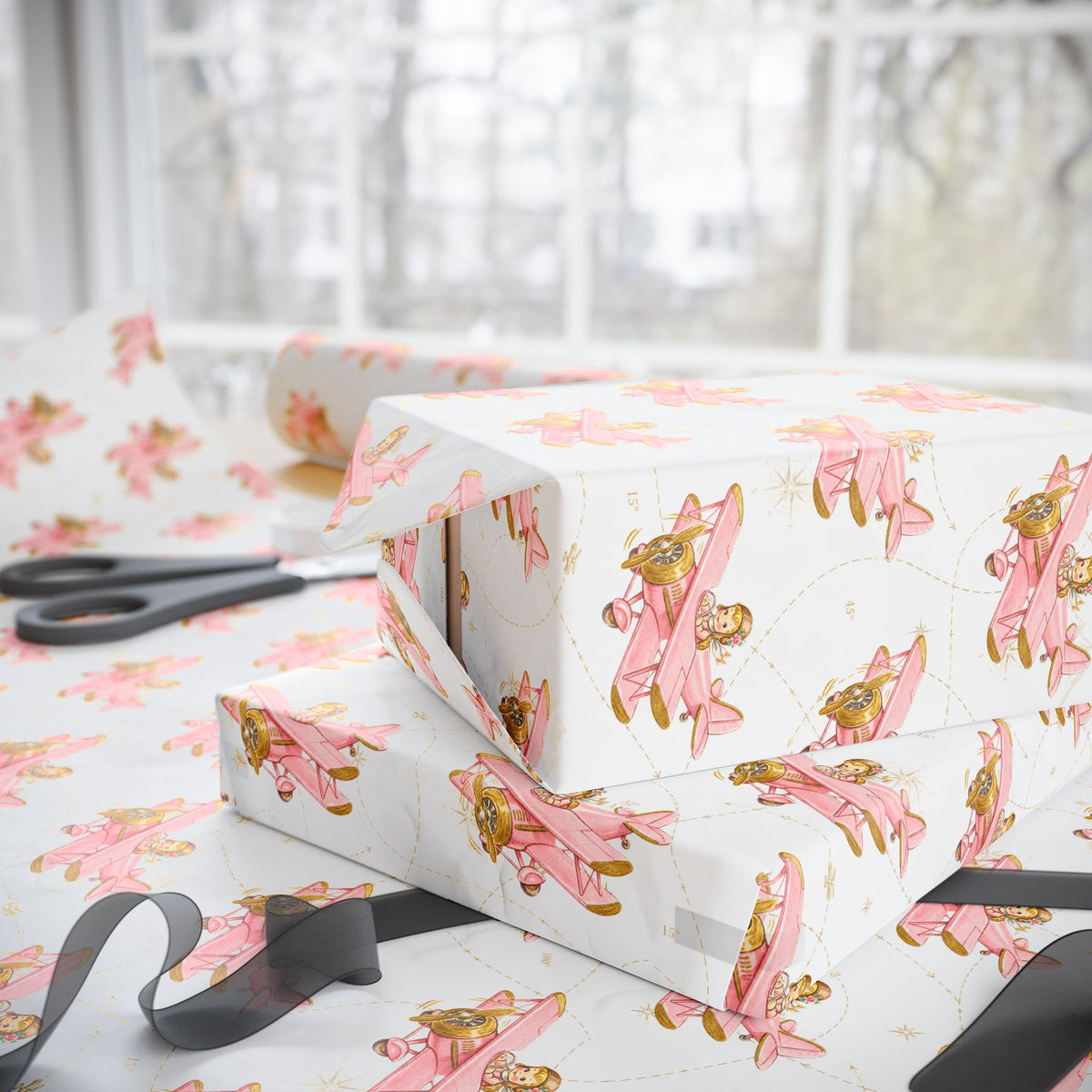 Gift boxes wrapped in paper featuring a little girl flying a pastel pink biplane over a delicate aviation navigation map on an ivory background, displayed with an open roll of matching wrapping paper, dark ribbon, and scissors.