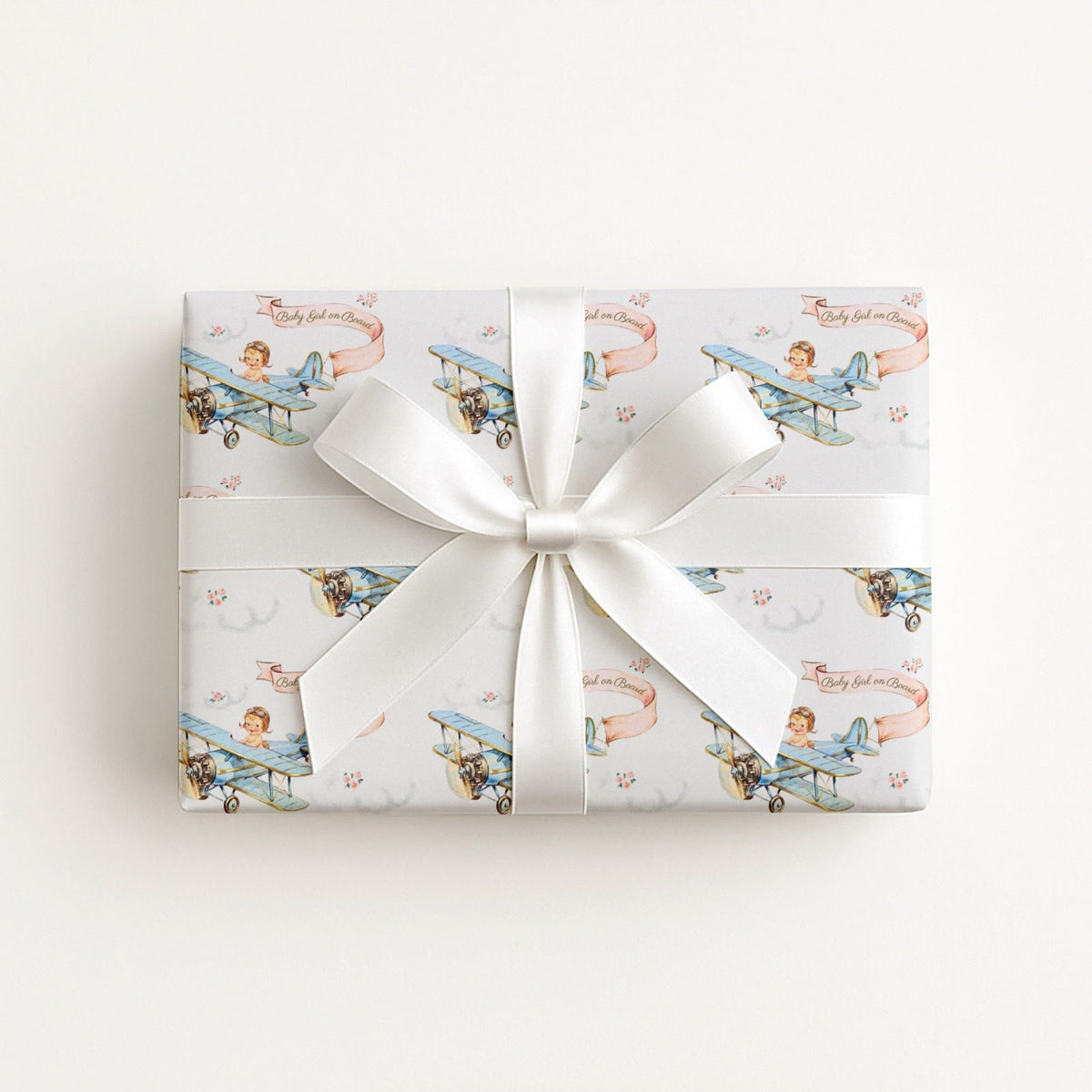 Baby Girl on Board airplane wrapping paper with a little girl aviator flying a vintage blue biplane with a pink banner on a soft white background.