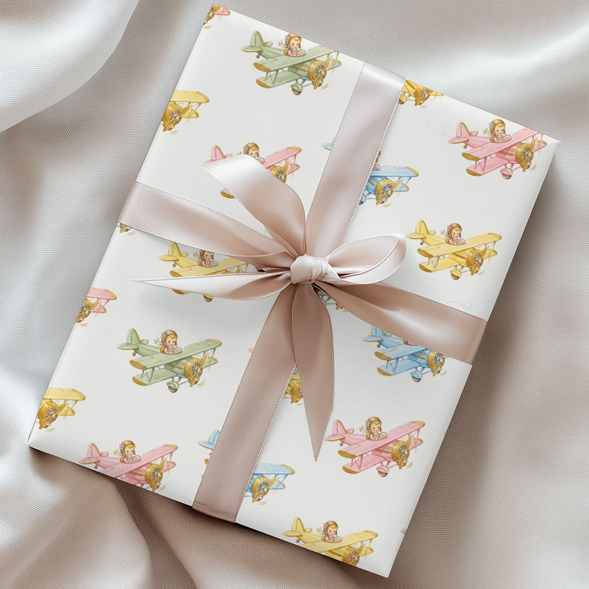 Gift box wrapped in paper featuring baby girls flying pastel airplanes tied with a satin ribbon.