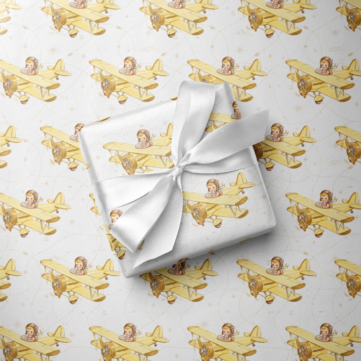Wrapped gift tied with a white satin bow, displayed on matching wrapping paper featuring a little girl flying a pale yellow biplane over a delicate navigation map with gold accents on an ivory background.
