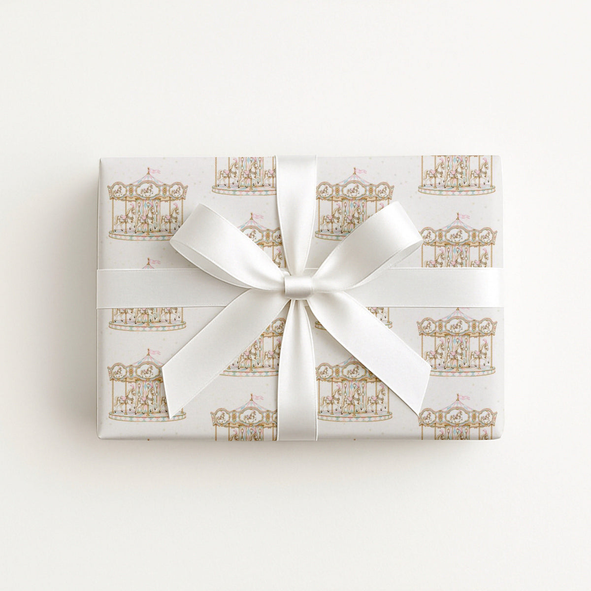 A rectangular gift box wrapped in white paper with a repeating gold carousel pattern and tied with a wide white satin ribbon bow, centered on a plain white background.