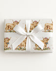 Gift box wrapped with baby wrapping paper featuring cow and baby illustrations on a light background.