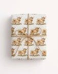 Gift wrapped in paper with highland cow and baby design on a light background.