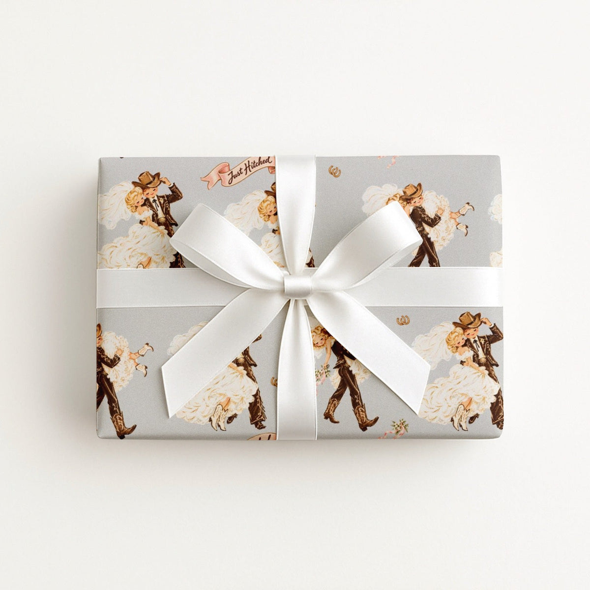 Western wedding wrapping paper with vintage cowboy groom and cowgirl bride, pink Just Hitched ribbons, and golden horseshoes.