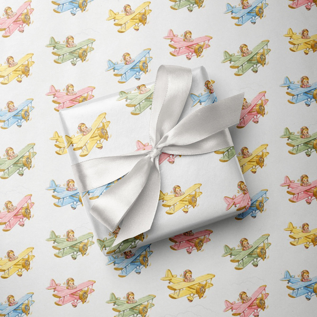 Gift wrapped in paper with pastel airplanes and girl pilot pattern, tied with a white ribbon.