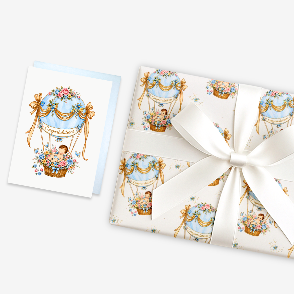New baby boy card with a baby in a blue floral hot air balloon beside matching blue hot air balloon baby shower wrapping paper tied with a ribbon