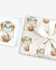 New baby boy card with a baby in a blue floral hot air balloon beside matching blue hot air balloon baby shower wrapping paper tied with a ribbon