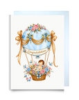 New baby boy card with a baby in a blue floral hot air balloon, golden ribbons and a Congratulations banner