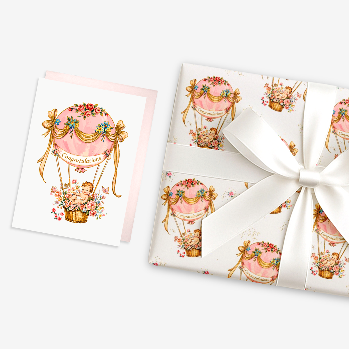 New baby girl card with a baby in a pink floral hot air balloon beside matching pink hot air balloon baby shower wrapping paper tied with a ribbon