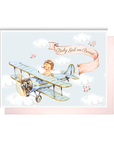 Vintage-style new baby girl card with a baby pilot in a blue biplane and a pink Baby Girl on Board banner among clouds
