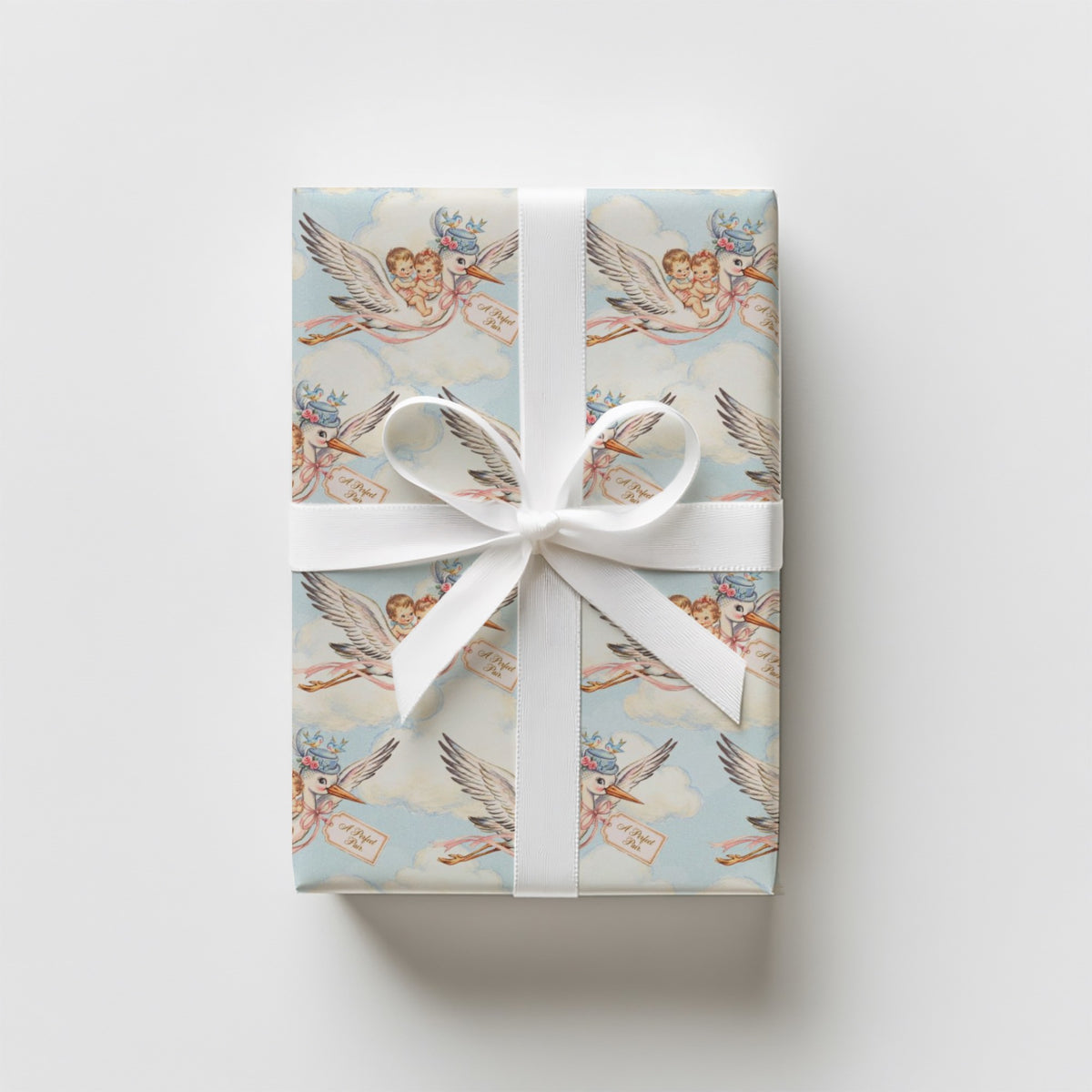 Upright gift wrapped in vintage-style twin baby shower wrapping paper with storks, a white satin ribbon and bow