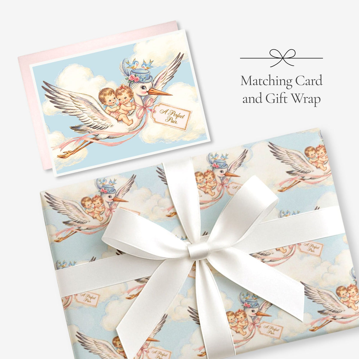 Twin baby boy and girl stork card with matching stork gift wrap tied with a white satin bow, labeled Matching Card and Gift Wrap