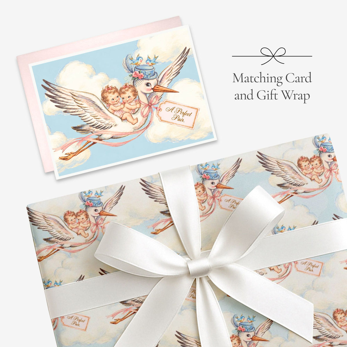 Twin girls stork card with matching twin girls stork gift wrap tied with a white satin bow, labeled Matching Card and Gift Wrap
