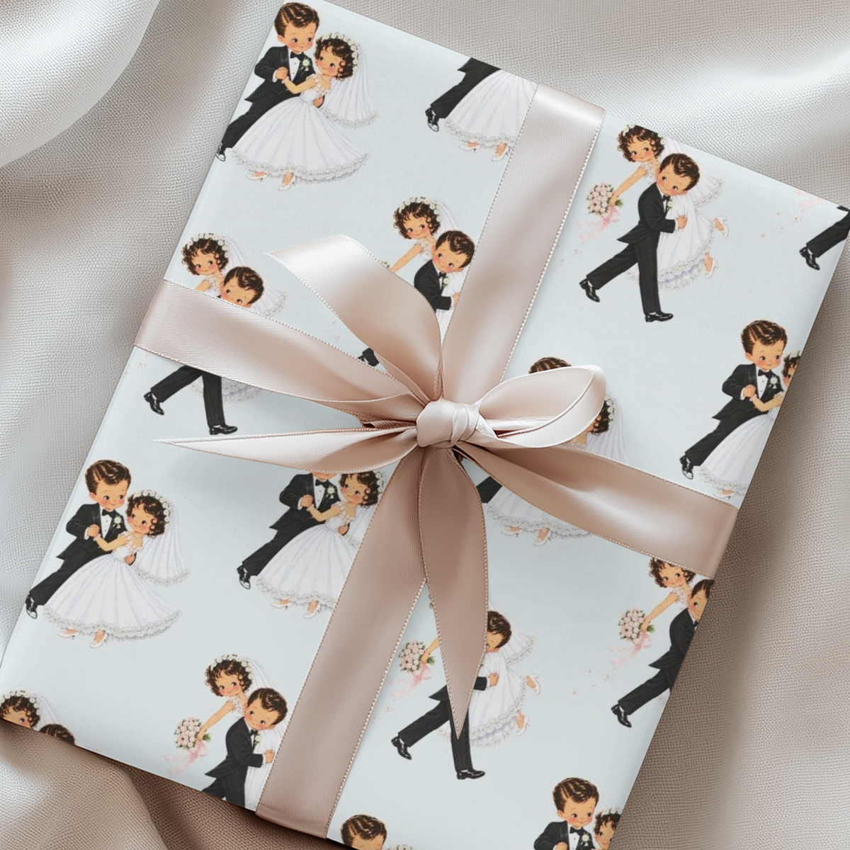 Gift wrapped in vintage-style bride and groom wedding wrapping paper on pale blue, tied with a blush satin ribbon and bow on soft fabric